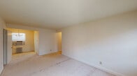 This single-floor residential unit offers a straightforward and functional layout, as visible in the dollhouse view. The living areas are finished with neutral-toned carpet flooring and cream-painted walls, creating a clean and understated aesthetic throughout. Windows in multiple rooms allow for natural light to filter in, contributing to a bright and airy feel.

The kitchen is equipped with a double-basin stainless steel sink, white laminate countertops, and wood-trimmed cabinetry offering ample storage both above and below the counter. The layout provides a practical workspace suitable for everyday use.

The bedrooms are generously proportioned, each featuring carpeted floors and individual closets with built-in shelving and hanging rods for organized storage. One bedroom includes a ceiling fan with integrated lighting, while radiator heating units positioned beneath the windows serve the living spaces, indicating a classic heating system.

The bathroom features a classic black-and-white mosaic tile floor, white wainscoting, and a window with blinds that provides natural light and ventilation. The space is clean and efficiently arranged.

Overall, this unit presents a functional and well-organized floor plan with consistent finishes throughout, offering a comfortable and livable environment with classic residential details.