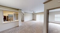 Located in Austin, TX, this well-appointed single-story residence offers four bedrooms, two bathrooms, and a thoughtfully designed layout. The open-concept living room is a welcoming centerpiece, featuring plush carpeting, crown molding, a ceiling fan with light fixture, and sliding glass doors dressed with vertical blinds that invite natural light and outdoor access. Built-in shelving near the kitchen pass-through adds both function and character to the shared living space. The kitchen is equipped with white shaker-style cabinetry, light countertops, a gray subway tile backsplash, stainless steel appliances including a range, microwave, dishwasher, and refrigerator, and durable wood-look flooring. The bedrooms are carpeted and bright, each featuring ceiling fans and window blinds for comfort and privacy. The primary bedroom includes a walk-in closet outfitted with wire shelving for organized storage. The bathrooms feature wood-look flooring, white vanities, and tiled shower surrounds. A dedicated laundry room houses a full-size washer and dryer with overhead shelving for added convenience. Neutral tones and clean finishes throughout create a cohesive and functional living environment.