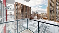 Located at 1215 5th Street SW in Calgary's vibrant Beltline neighbourhood, this three-bedroom, one-bathroom unit offers a well-designed layout across a single floor. The interior features warm hardwood flooring throughout the living areas and bedrooms, complemented by crisp white walls that create a bright, clean aesthetic. Large floor-to-ceiling windows flood the space with natural light while framing sweeping views of the surrounding Calgary cityscape — a standout feature of the unit. The kitchen is outfitted with stainless steel appliances, white cabinetry, a tiled backsplash, and a generous granite-topped island with an integrated sink, making it both functional and visually appealing. The primary bedroom benefits from expansive windows with direct city views, offering an airy and open feel. The bathroom is finished with large-format grey floor tiles, a wood-toned vanity with ample storage, a full-size soaker tub, and white subway-tiled surround. A private balcony with glass railings extends the living space outdoors, providing panoramic views of the downtown Calgary skyline and surrounding neighbourhood rooftops — ideal for taking in the urban landscape year-round.