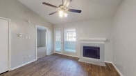 This single-floor residence offers a thoughtfully designed layout with a blend of comfort and modern finishes. The living area immediately impresses with its vaulted ceilings, a ceiling fan with integrated lighting, and rich wood-look flooring that flows seamlessly underfoot. A tiled fireplace with a clean white mantel serves as the room's focal point, while a glass door and adjacent windows invite generous natural light and outdoor views. The entryway opens into a spacious living and dining area, with pendant lighting above and a pass-through to the kitchen, creating an open, connected feel. The kitchen features crisp white cabinetry, granite countertops, wood-look flooring, and black appliances including a dishwasher, range, and refrigerator, offering both style and functionality. The bedrooms are carpeted for comfort and feature vaulted ceilings and large windows that frame outdoor views, filling the rooms with natural light. The bathrooms are finished with granite-topped white vanities, dark-framed mirrors, and a tiled shower-tub combination, reflecting a consistent attention to detail. Neutral tones throughout the home create a calm, welcoming ambiance suited to a variety of living styles.