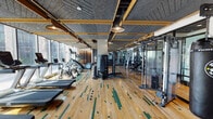 Located at 845 W Madison St in Chicago's West Loop neighborhood, this fitness center is a comprehensively appointed facility designed to support a full range of workout routines. The space is unified by a striking hardwood floor featuring a distinctive green-striped pattern, adding a dynamic visual element throughout. A textured acoustic ceiling with gold-toned structural beams runs the length of the facility, complemented by pendant lighting that creates a warm yet functional atmosphere.

Floor-to-ceiling windows line one side of the main workout area, flooding the space with natural light and offering views of the surrounding urban streetscape. The cardio section is well-stocked with treadmills, stationary bikes, ellipticals, and stair climbers, all positioned to take advantage of the exterior views. On the opposite side, a robust strength training zone features cable machines, power racks, free weights, and multi-station equipment, with mirrored walls enhancing the sense of depth and supporting proper form.

A separate studio room provides a dedicated space for functional training and flexibility work, equipped with stability balls, medicine balls, resistance tools, and an interactive fitness display. The studio's mirrored walls and open floor plan make it well-suited for stretching, group exercise, or personal training sessions. Together, these areas form a cohesive, modern fitness environment.