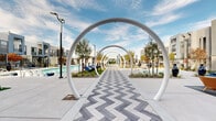 The Elysian community's outdoor amenity space is a masterfully designed gathering environment that combines bold architectural elements with resort-style leisure features. A signature chevron-patterned paver walkway serves as the central spine of the space, framed by a dramatic series of repeating white circular arches that create a striking visual corridor drawing residents through the heart of the amenity area.

Flanking the central walkway are two pools — a spacious lap pool and a separate recreational pool — each surrounded by wide concrete decking and lined with chaise lounges positioned on patches of synthetic turf, offering an inviting place to relax under open skies. Landscaped beds with native-style plantings and ornamental trees punctuate the hardscape throughout, adding natural texture and shade.

A covered outdoor lounge area features vibrant, stylishly curated seating arrangements, including woven furniture and accent chairs in bold blue and orange tones, set against a backdrop of the contemporary multi-story buildings that define the community's modern aesthetic. Bold orange columns frame the building entry, accented by large sculptural vases.

An outdoor recreation zone shaded by sail canopies offers a ping pong table, café-style seating, string lights, and an outdoor screen, making it ideal for casual social gatherings. Together, these elements create a dynamic, amenity-rich outdoor environment designed for community living.