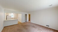 This single-floor residence offers a practical and comfortable layout across two bedrooms, one bathroom, a living room, kitchen, hallway, and dedicated closet space. The living room is bright and welcoming, featuring neutral carpet flooring and a large window that fills the space with natural light and views of surrounding greenery. A front entry door opens directly into this generous living area, creating an inviting first impression.

The kitchen is efficiently designed with white cabinetry extending to the ceiling for ample storage, light wood-style flooring, white appliances including a refrigerator and electric range, and a window above the sink that brings in natural light. A pass-through counter connects the kitchen to the adjacent living area.

Both bedrooms are carpeted and finished in clean white tones. Each features a built-in closet with bi-fold doors and hanging rods, providing practical storage. The bedrooms receive natural light through windows with vertical blinds, offering views of the outdoors. The primary bedroom is comfortably sized with its own walk-in style closet visible through an open doorway.

The bathroom is finished with white subway tile on the walls and tub surround, a granite-topped vanity with a framed mirror, and a window for natural ventilation. The overall aesthetic throughout is clean, neutral, and move-in ready.