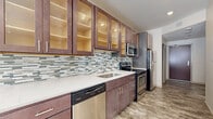 Located on East Sixth Street in Cleveland, Ohio, this single-floor unit showcases a clean, modern aesthetic with thoughtfully designed interiors. The galley-style kitchen is a standout feature, offering rich dark-stained cabinetry with glass-front upper cabinets that are internally lit, highlighting their textured interiors. A mosaic glass tile backsplash in muted blues and greens adds visual interest, complementing the white quartz countertops. Stainless steel appliances, including a range, microwave, dishwasher, and refrigerator, complete the functional and stylish kitchen.

The living and dining areas are bright and airy, benefiting from large windows that allow natural light to fill the space. Stone-look tile flooring flows throughout, providing a neutral, durable foundation that ties the rooms together. A pendant light fixture adds a refined touch to the dining area, which connects seamlessly to the kitchen peninsula.

A secondary room, framed by large windows with exterior views, offers flexible use as a bedroom or office. The bathroom features a glass-enclosed walk-in shower with white subway tile, a dark-stained vanity with a stone countertop, and neutral floor tiles, delivering a clean, spa-like finish. Overall, the unit presents a polished, contemporary living environment.
