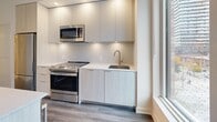 Located in Toronto, Ontario, this thoughtfully laid-out 2-bedroom, 2-bathroom unit offers a clean, contemporary aesthetic across a single floor. The open-concept kitchen is a standout feature, equipped with stainless steel appliances including a gas range, built-in microwave, and full-size refrigerator. Flat-panel cabinetry in a light wood finish is paired with a stone-look backsplash and a white quartz countertop that extends to a peninsula — ideal for casual dining or meal prep. Hardwood-style flooring runs throughout the living areas and bedrooms, adding warmth and continuity to the space. The primary bedroom is a comfortable, private retreat with a window offering views of the surrounding urban streetscape. The second bedroom is equally bright, benefiting from natural light through a large window. Two well-appointed bathrooms serve the unit: one features a glass-enclosed walk-in shower with large-format tile surround, while the second includes a soaker tub with matching tile finishes and chrome fixtures. Three hallways connect the rooms efficiently, contributing to a practical and logical floor plan. The overall palette — white walls, light cabinetry, and neutral flooring — gives the unit a fresh, modern feel throughout.