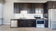 Located at 20 W Northwest Hwy in Mount Prospect, IL, this well-designed single-floor unit offers a thoughtfully laid-out living space with modern finishes throughout. The open-concept kitchen is a standout feature, showcasing rich dark cabinetry with brushed nickel hardware, white quartz countertops, a classic subway tile backsplash, and a full suite of stainless steel appliances including a French door refrigerator, electric range, over-the-range microwave, and dishwasher. The kitchen flows seamlessly into the main living area, which is finished with durable wood-look flooring that adds warmth and continuity to the space. The bedrooms are carpeted for comfort and feature large windows that invite natural light and offer views of the surrounding neighborhood, as well as built-in closets providing ample storage. The unit includes two bathrooms: one full bathroom with a soaking tub and tiled surround, and a second bathroom featuring a sleek walk-in glass-door shower. Both bathrooms are finished with dark-framed vanity mirrors, dark wood cabinetry, white countertops, and wood-look flooring, creating a cohesive, contemporary aesthetic. Overall, the unit presents a clean, modern ambiance with a neutral color palette throughout.