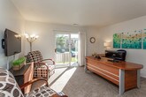 This single-floor residence offers a functional and comfortable layout across several well-defined rooms. The living area is carpeted and filled with natural light, anchored by a sliding glass door that opens to an outdoor patio with views of the surrounding grounds. A wall-mounted television and seating area create a relaxed atmosphere, while an adjoining space accommodates a desk and additional seating, making it suitable as a home office or multipurpose area.

The kitchen features warm honey-toned wood cabinetry, a double sink, and white appliances including a range, dishwasher, and refrigerator. A dining table positioned nearby provides a convenient space for meals. Open shelving along one wall adds additional storage and display options, and tile flooring runs throughout this area.

Both bedrooms are carpeted and receive natural light through large windows. Each includes a double-door closet and offers a comfortable, well-proportioned sense of space. A dedicated office or flex room also features a large window and carpet, providing a quiet and productive environment.

The two bathrooms are clean and practical. One includes a vanity with wood cabinetry and a mirror, while the other features a full tub-and-shower combination with white tile surround. Throughout the unit, neutral walls and consistent finishes create a cohesive and welcoming ambiance.