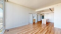 Located on a high floor at 1820 Minor Ave in Seattle's vibrant South Lake Union neighborhood, this modern one-bedroom, one-bathroom unit offers a thoughtfully designed open-concept layout with clean contemporary finishes throughout. The combined living and kitchen area is anchored by warm hardwood-style flooring and dramatic floor-to-ceiling windows that flood the space with natural light and frame sweeping views of the Seattle skyline and surrounding cityscape. The kitchen is well-appointed with stainless steel appliances including a gas range, microwave, and refrigerator, complemented by warm wood lower cabinetry, white upper cabinets, a large island with a white quartz countertop, an undermount sink, and pendant lighting overhead. Track lighting provides additional illumination throughout the space. The bedroom features plush carpeting, a floor-to-ceiling window with city views, an exposed concrete structural column adding an industrial accent, and access to a dedicated closet. The bathroom is finished with large-format tile flooring, a wood-toned vanity with white countertop, a wide mirror, and a bathtub. A hallway connects all rooms, completing this efficient and stylish urban residence.