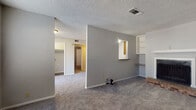 Located at 1900 Kickingbird Road in Edmond, Oklahoma, this single-floor residence offers a practical and comfortable layout throughout. The living room serves as the central gathering space, featuring a brick-hearth fireplace with a white mantle, built-in shelving, and a pass-through window that connects to an adjacent area, adding both functionality and character. Soft carpet flooring and textured walls are consistent throughout the living spaces, contributing to a cozy atmosphere. A ceiling fan with integrated lighting is installed in the bedroom, which also benefits from a window fitted with blinds that allows natural light to filter in. The kitchen is equipped with warm wood cabinetry, laminate countertops, and a double sink, and it opens toward a living or dining area through a half-wall peninsula. A sliding glass door at the far end of this area provides access to the outdoors and brings in additional natural light. The bathroom features a full tub-shower combination with white tile surround, maintaining a clean and functional design. Throughout the home, textured ceilings, neutral wall tones, and consistent carpeting create a unified and understated aesthetic well-suited for everyday living.