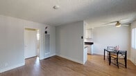 This single-floor unit offers a functional and comfortable layout designed for everyday living. The open-concept living and dining area is finished with warm wood-look flooring, neutral gray walls, and a textured ceiling throughout. A ceiling fan keeps the dining space comfortable, while a large window fitted with vertical blinds fills the area with natural light and offers views of the surrounding exterior. The living space flows seamlessly toward the kitchen pass-through, creating an airy, connected feel.

The galley-style kitchen is efficiently designed with ample cabinetry in a clean gray-white finish, dark countertops, a double stainless steel sink, a gas range, and a stainless steel refrigerator. A skylight provides additional brightness to the workspace, making it a practical and pleasant area to cook.

The bedroom features soft carpeting, neutral walls, and a window with vertical blinds that bring in natural light while maintaining privacy. The room offers a calm, restful atmosphere with a clean, simple layout.

The bathroom is neatly appointed with a vanity featuring a wide countertop, white under-sink cabinetry, chrome fixtures, and well-lit mirrors. The shower area is enclosed with a curtain, completing the functional design of the space.