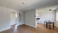 This single-floor unit offers a functional and comfortable layout designed for everyday living. The open-concept living and dining area is finished with warm wood-look flooring, neutral gray walls, and a textured ceiling throughout. A ceiling fan keeps the dining space comfortable, while a large window fitted with vertical blinds fills the area with natural light and offers views of the surrounding exterior. The living space flows seamlessly toward the kitchen pass-through, creating an airy, connected feel.

The galley-style kitchen is efficiently designed with ample cabinetry in a clean gray-white finish, dark countertops, a double stainless steel sink, a gas range, and a stainless steel refrigerator. A skylight provides additional brightness to the workspace, making it a practical and pleasant area to cook.

The bedroom features soft carpeting, neutral walls, and a window with vertical blinds that bring in natural light while maintaining privacy. The room offers a calm, restful atmosphere with a clean, simple layout.

The bathroom is neatly appointed with a vanity featuring a wide countertop, white under-sink cabinetry, chrome fixtures, and well-lit mirrors. The shower area is enclosed with a curtain, completing the functional design of the space.