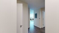 This thoughtfully designed 2-bedroom, 2-bathroom residence on a single floor offers a modern and cohesive living experience. The open-concept kitchen features two-tone dark and white cabinetry, stainless steel appliances including a refrigerator, range, and microwave, a subway tile backsplash, and a central island with light countertops — ideal for both cooking and casual dining. Rich hardwood flooring flows throughout the main living areas, connecting the kitchen seamlessly to the living room, where floor-to-ceiling corner windows frame sweeping panoramic city and treetop views, filling the space with abundant natural light. The primary bedroom continues this elevated aesthetic with a large picture window overlooking the urban skyline, complemented by hardwood-style flooring. The second bedroom is comfortably sized and warmly appointed. Both bathrooms are finished with contemporary dark wood vanities and white countertops; one features a glass-enclosed walk-in shower with marble-style tile flooring, while the other includes a full soaking tub with white subway tile surround. A dedicated in-unit laundry room houses a full-size washer and dryer. Two hallways provide smooth connectivity throughout, and a private balcony extends the living space outdoors.