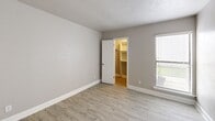 Located at 7879 Riverfall Dr in Dallas, TX, this one-bedroom, one-bathroom unit offers a thoughtfully designed single-floor layout. Light wood-style flooring flows throughout the space, complementing the neutral gray and white color palette that creates a clean, modern aesthetic.

The open-concept living, dining, and kitchen area forms the heart of the unit. The kitchen features white cabinetry, granite-look countertops, black appliances including a refrigerator and range, and a peninsula with a built-in sink — providing both functionality and a natural dining counter. A washer is conveniently integrated into the kitchen cabinetry. Pendant lighting illuminates the kitchen area, while natural light pours into the living room through vertical blinds leading to a private patio.

The bedroom offers a comfortable footprint with access to a walk-in closet, providing ample storage. A second closet adds further organizational flexibility. The full bathroom is well-finished with a granite-topped vanity, white cabinetry, a framed mirror, and a tub/shower combination with white tile surround.

Throughout the unit, white baseboards and trim provide crisp contrast against the neutral walls, and updated light fixtures add a polished touch. The patio extends the living space outdoors, rounding out this efficient and functional Dallas residence.