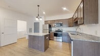 This single-floor residence offers a thoughtfully designed layout that balances functionality and comfort. The kitchen serves as the centerpiece of the home, showcasing rich medium-toned wood cabinetry, granite-style countertops, and a full suite of stainless steel appliances including a refrigerator, electric range, microwave, and dishwasher. A central island with a matching countertop provides additional prep space and a casual gathering point. Light hardwood-style flooring and a pendant chandelier add warmth to the kitchen area, which also benefits from vaulted ceilings that enhance the sense of openness.

The bedrooms are generously sized, finished with plush neutral carpeting and bright white walls that maximize the natural light pouring in through large windows overlooking lush greenery. One bedroom opens directly to a private balcony accessible via a sliding glass door, while a ceiling fan overhead ensures year-round comfort. Closet space is well provided, with a sliding-door closet visible in one of the bedrooms.

The bathroom features a full tub-shower combination with clean white finishes and wood-style flooring. A dedicated in-unit laundry area with a full-size washer and dryer adds a practical convenience. Throughout, the space maintains a clean, modern aesthetic with neutral tones and well-considered details.