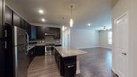 This single-floor residence offers a well-designed open-concept layout that seamlessly connects the kitchen and living area. The kitchen is a standout feature, showcasing dark espresso-toned cabinetry that extends to the ceiling, a neutral tile backsplash, and granite countertops. A central island with matching granite provides additional prep and seating space, illuminated by sleek pendant lighting. Stainless steel appliances, including a refrigerator, range, dishwasher, and microwave, complete the modern kitchen aesthetic. The open living area flows naturally from the kitchen, featuring wood-style flooring, recessed lighting, and a ceiling fan that adds both function and style. The bedrooms offer a calm, neutral palette with warm wood-style floors and windows with blinds that allow for natural light. The primary bathroom is well-appointed with a framed glass walk-in shower, dark vanity cabinetry, granite countertops, and a tall linen storage tower. A secondary full bathroom mirrors the refined finishes with matching dark cabinetry, granite countertops, and a tiled tub-shower combination. Throughout the space, consistent use of wood-style flooring, neutral wall tones, and cohesive dark cabinetry creates a unified and contemporary ambiance.