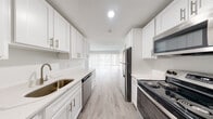 This studio unit at Coleman Towers offers a well-designed, single-floor layout that makes efficient use of its compact footprint. The galley-style kitchen is a standout feature, outfitted with crisp white shaker cabinetry, brushed nickel hardware, quartz countertops, and a full suite of stainless steel appliances including a refrigerator, electric range, microwave, and dishwasher. Abundant upper and lower cabinet storage lines both sides of the kitchen, providing generous organization space. Light wood-style luxury vinyl flooring runs throughout the unit, lending a clean, cohesive aesthetic. The open living area is bright and airy, anchored by a wide sliding glass door with vertical blinds that allows natural light to fill the space and provides access to outdoor views. The bathroom is finished with white subway tile in the walk-in shower, a white vanity with quartz countertop, and coordinating brushed nickel fixtures and grab bars. The entrance area flows directly from the kitchen, keeping the layout intuitive and accessible. With its modern finishes, neutral color palette, and thoughtfully arranged spaces, this unit offers a clean and functional living environment within Coleman Towers.