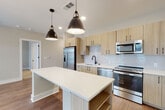 This single-floor residence showcases a thoughtfully designed open-concept layout that seamlessly connects the kitchen, dining, and living areas. The kitchen is a standout feature, outfitted with light wood cabinetry, white quartz countertops, a white subway tile backsplash, and a full suite of stainless steel appliances including a French door refrigerator, range, microwave, and dishwasher. A generously sized center island with built-in shelving provides additional prep space and storage, while two matte black industrial-style pendant lights add a modern accent overhead. The living area extends naturally from the kitchen, bathed in natural light from large windows fitted with blinds and accented by a sputnik-style chandelier.

The bedrooms feature plush carpeting, ceiling fans, and large windows that invite abundant natural light. Two well-appointed bathrooms mirror the home's contemporary aesthetic, each featuring light wood vanities with white quartz countertops and black hardware accents. One bathroom includes an illuminated backlit mirror and direct access to a walk-in closet. A clean hallway with built-in hooks and recessed lighting connects the rooms, and wood-look flooring runs throughout the main living spaces, tying the design together cohesively.