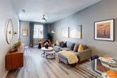 This single-story unit offers a thoughtfully organized layout across a comfortable footprint, incorporating a combined kitchen and living room, one bedroom, one bathroom, a hallway, and a private balcony. The open-concept living and kitchen area forms the heart of the space, where light wood-style flooring, neutral gray walls, and recessed lighting establish a clean, contemporary aesthetic. The living area accommodates a generous seating arrangement beneath a ceiling fan, with a window dressed in floor-length drapes allowing natural light to fill the room.

The kitchen is equipped with stainless steel appliances, including a range, microwave, and refrigerator, complemented by white shaker-style cabinetry, a tile backsplash, and light quartz countertops that extend to a peninsula — ideal for casual dining or meal prep.

The bedroom is a well-proportioned retreat finished with plush carpeting, soft sage-toned walls, a window with natural light, and wall space suited for artwork and décor. The bathroom features a white floating vanity with quartz countertop, an undermount sink, and wood-style flooring, maintaining the unit's clean, modern character throughout. A private balcony provides additional outdoor living space.
