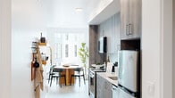 This thoughtfully designed single-floor residence combines contemporary finishes with functional living spaces. The galley-style kitchen runs along one side of the unit, outfitted with wood-toned cabinetry, white quartz countertops, stainless steel appliances including a range, dishwasher, and refrigerator, as well as open shelving for additional storage. Light wood-look flooring flows continuously throughout, unifying the space with a clean, modern aesthetic.

A dedicated in-unit laundry closet houses a stacked washer and dryer, offering a practical convenience tucked neatly out of sight. The hallway transitions seamlessly into the combined living and dining area, where large windows draw in generous natural light and frame neighborhood views of the surrounding cityscape. The dining area accommodates a round table with ample seating, while the living room benefits from multiple tall windows that further brighten the space.

The bedroom is a calm, well-appointed retreat with clean white walls and closet storage. The full bathroom features white tile surround with a soaking tub and shower combination, complemented by chrome fixtures. Throughout the residence, recessed lighting, a neutral color palette, and contemporary finishes create a cohesive, modern living environment.