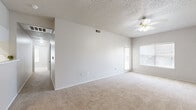 Located at 7500 Rolling Brook Dr in Frisco, TX, this single-story home offers four bedrooms and two full bathrooms within a well-organized floor plan. The entry opens into a living area finished with plush carpet and transitions seamlessly to hardwood-style flooring toward the front door, with a textured ceiling and recessed lighting adding subtle detail. The living room is spacious and bright, featuring a ceiling fan and a large window that invites natural light. The galley-style kitchen runs parallel counters lined with white cabinetry, marble-look countertops, and black appliances including a range and refrigerator, complemented by hardwood-style flooring and a circular overhead light fixture. The four bedrooms are carpeted and finished in neutral tones, each offering a quiet, versatile space. Several bedrooms include ceiling fans and windows with blinds that allow for natural light and outdoor views. Both bathrooms feature hardwood-style flooring, white vanities with marble-look countertops, and tub-shower combinations with curtains. A connecting hallway ties the bedrooms and bathrooms together efficiently. Throughout, the home maintains a clean, neutral palette that provides a functional and adaptable living environment.