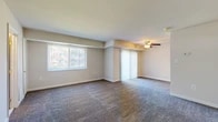 This two-floor residence offers a practical and comfortable layout spread across two levels. The main living area is generously proportioned, featuring wall-to-wall carpet and a ceiling fan with light fixture overhead. Large windows dressed with vertical blinds allow ample natural light to fill the space, while a sliding glass door leads to an adjacent area, creating an open and connected feel between rooms.

The galley-style kitchen is efficiently designed with warm wood cabinetry lining both sides, dark granite-look countertops, wood-look flooring, and white appliances including a gas range, over-the-range microwave, and refrigerator. A half bathroom on one level provides a vanity with wood cabinetry and a wall mirror, while the full bathroom on the upper level includes a tub-shower combination with white tile surround.

The bedrooms are carpeted and feature mirrored sliding closet doors that reflect light and enhance the sense of space. Windows in each bedroom bring in natural light. A staircase connects the two floors, and an additional room with mirrored closet doors offers flexible use. Throughout, neutral beige tones and clean white trim create a calm, understated ambiance.