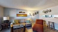 This two-bedroom, one-bathroom residence in Memphis, Tennessee presents a thoughtfully arranged single-floor layout that maximizes functionality and comfort. The living room features wood-look flooring, a textured ceiling, and neutral gray walls that create a warm, welcoming atmosphere, with a window providing natural light and views to the exterior. Adjacent to the living area, a dedicated dining space accommodates a full dining set and is accented by decorative wall art, making it ideal for everyday meals or entertaining. The galley-style kitchen is efficiently organized with white cabinetry, marble-look countertops, stainless steel appliances including a refrigerator and dishwasher, and a window that brings in additional natural light. Both bedrooms are carpeted and feature soft gray walls, natural light from windows with blinds, and walk-in closets that provide ample storage. The primary bedroom is particularly spacious, offering room for a full furniture suite. The full bathroom includes a tiled shower-tub combination and clean white fixtures. Throughout the unit, consistent wood-look flooring in the main living areas and plush carpet in the bedrooms contribute to a cohesive and comfortable living environment.