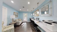 Located at 1 Westchase Dr in Charleston, SC 29407, this single-story space serves as a polished and functional business center or leasing office. The interior is defined by soft sky-blue walls that create a calm, professional atmosphere, complemented by rich dark hardwood flooring that adds warmth and contrast throughout.

The main room features a long built-in countertop workstation along one wall, equipped with multiple computer terminals and task lighting provided by elegant pendant lights hanging above. Recessed ceiling lights offer even illumination across the space. A comfortable seating area with a neutral-toned sofa and an accent armchair in a botanical print provides a welcoming area for visitors or clients.

Natural light flows generously into the space through both a glass-paned single door and a set of French double doors, offering views of the surrounding exterior and enhancing the open, airy feel of the room. Decorative landscape artwork in wood frames adorns the walls, reinforcing the inviting and tasteful aesthetic. A geometric wire mirror accent adds a contemporary touch to the decor.

Overall, this space balances practical office functionality with a refined, hospitable design that is well-suited for client-facing interactions or administrative work in the Charleston area.