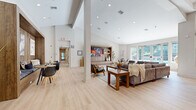 Located at 9001 Renner Blvd in Lenexa, Kansas, this single-floor community space offers a thoughtfully designed, open-plan layout that seamlessly connects a lounge, dining, and kitchen area. Light oak hardwood flooring runs throughout, creating a warm and cohesive aesthetic that ties the entire space together.

The expansive lounge area is anchored by a built-in wood-paneled entertainment wall with integrated shelving and a large mounted display. Generous seating arrangements, including a plush sectional sofa and mid-century modern accent chairs, are centered around a wood coffee table atop a textured area rug. Recessed lighting and elevated ceilings amplify the sense of openness, while large windows and glass doors flood the interior with natural light and offer views of the outdoor surroundings.

A dedicated dining zone features a sleek dining table with contemporary chairs, set beneath a warm wood-framed architectural accent wall that adds depth and character to the room.

The kitchen is a standout feature, showcasing bold large-format hexagonal tile on a dramatic accent wall, paired with crisp white shaker cabinetry with matte black hardware, a stone-topped island with bar seating, stainless steel appliances, open wood floating shelves, and a black undermount sink. The overall ambiance is modern, welcoming, and well-appointed throughout.