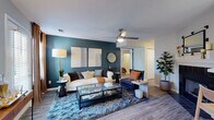 This thoughtfully designed single-floor residence offers a cohesive blend of modern style and comfortable living across several well-appointed spaces. The living room serves as the centerpiece of the home, featuring a striking deep teal accent wall adorned with large-format artwork, wood-look flooring, a ceiling fan with integrated lighting, and a tiled fireplace surround — creating a warm yet contemporary atmosphere. The space flows naturally into a dedicated dining area, which is brightened by a window dressed with warm-toned curtains and anchored by a pendant chandelier overhead. The kitchen is efficiently laid out with white upper cabinetry, contrasting lower cabinetry, white subway tile backsplash, light countertops, and stainless steel appliances including a range and dishwasher. Two bedrooms each carry their own distinct character: one features a rich terracotta accent wall with plush carpeting and natural light from large windows, while the other showcases a deep blue accent wall, ceiling fan, and carpeted flooring. The bathroom is finished with wood-look tile flooring, a vanity with under-sink cabinetry, and a shower-tub combination. Throughout the residence, consistent flooring, neutral base tones, and vibrant accent walls unify the overall design.