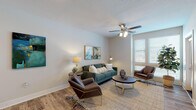 This single-floor residence is thoughtfully designed with a contemporary aesthetic and a practical, open layout. The living area serves as the heart of the home, featuring wood-style plank flooring, neutral walls, and a ceiling fan. A large window allows natural light to fill the space, creating a bright and welcoming atmosphere.

The kitchen flows seamlessly into the living area and is equipped with dark espresso cabinetry, a white quartz countertop island with a double undermount sink, stainless steel appliances including a refrigerator and dishwasher, a subway tile backsplash, and pendant lighting overhead. The island offers seating for multiple guests, making it an ideal space for both casual dining and entertaining.

The bedroom is generously sized, featuring plush carpeting, multiple windows with blinds, a ceiling fan, and direct access to a private bathroom. The bathroom is finished with wood-style flooring, a tub-shower combination with white subway tile surround, a dark vanity with a white countertop, an undermount sink, and a large mirror. The overall design maintains a cohesive modern palette, combining dark cabinetry accents with crisp white surfaces throughout.
