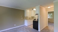 This single-floor residence offers a straightforward and functional layout designed to maximize usability. The open-concept living area flows directly into the kitchen, creating a connected and accessible space. The living area features neutral-toned carpeting and warm tan-painted walls, lending a cozy and welcoming ambiance throughout.

The kitchen is outfitted with crisp white cabinetry that extends to the upper and lower sections, providing ample storage. A decorative mosaic tile backsplash adds a subtle design accent, complementing the light-toned countertops. Black appliances, including a range and an under-cabinet range hood, provide a contemporary contrast to the white cabinetry. A stainless steel sink is centrally positioned beneath overhead cabinets, offering practical workspace.

The textured popcorn ceiling runs throughout the space, while clean white baseboards frame the floors. The layout is defined by a partial wall that separates the kitchen from the living area, creating a sense of structure without fully closing off the two spaces. Overall, the unit presents a clean, move-in-ready environment with a neutral palette that offers versatility for personalization.