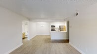 This single-floor unit offers a thoughtfully arranged layout encompassing three bedrooms, two bathrooms, a living room, and a hallway. The open-concept living and kitchen area serves as the heart of the home, featuring light-toned wood-style flooring, neutral gray-white walls, and a textured ceiling throughout. The kitchen is positioned at one end of the main living space and is equipped with white upper cabinetry, stainless steel appliances including a refrigerator and microwave, and a raised breakfast bar that separates it from the living area. The living room is bright and airy, benefiting from a sliding glass door that opens to an outdoor area and allows natural light to fill the space. The three bedrooms are each finished with the same wood-style flooring and neutral tones, maintaining a clean and consistent aesthetic. The primary bedroom offers a comfortable footprint, while the additional bedrooms feature windows with exterior views and closet storage. Both bathrooms are functional and cleanly designed, each featuring a combined tub and shower unit with tiled surrounds, wood-toned vanity cabinetry, and brushed nickel fixtures. A connecting hallway links the bedrooms and bathrooms, providing an efficient and organized flow throughout the unit.