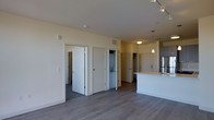 This single-floor residence offers a clean, contemporary design centered around an open-concept living area with smooth hardwood-style flooring throughout. The main living space is bright and airy, with neutral warm-white walls that contribute to the overall sense of openness. A kitchen peninsula anchors one end of the space, illuminated by pendant lighting that hangs from above, complementing the track lighting installed along the ceiling. Stainless steel appliances are visible in the kitchen area, adding a modern touch to the functional layout.

Multiple doors line the main living area, providing access to additional rooms and utility spaces. An in-unit stacked washer and dryer is tucked neatly into a dedicated closet, offering added convenience. The layout is thoughtfully organized, with clearly defined zones for living, cooking, and utility functions. Ceiling-mounted light fixtures provide consistent illumination throughout. The neutral color palette, combined with the contemporary flooring and modern fixtures, gives the space a clean and move-in-ready feel that is both practical and visually cohesive.