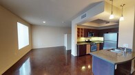 This single-floor space showcases a thoughtfully designed open-concept layout that seamlessly connects the kitchen and living areas. The polished concrete floors, featuring natural variation in tone and texture, serve as a striking design element throughout, adding an industrial yet refined character to the interior.

The kitchen is well-appointed with dark espresso cabinetry, granite countertops, and a full suite of stainless steel appliances, including a gas range, microwave, and refrigerator. Open shelving units provide convenient display and storage space, complementing the upper and lower cabinetry. A kitchen island with a granite countertop extends the workspace and offers a natural partition between the kitchen and the living area.

The living area is generously proportioned, offering a blank canvas for various furniture arrangements. Neutral-toned walls and recessed lighting contribute to a clean, modern aesthetic. HVAC vents are integrated into the ceiling, ensuring climate comfort throughout. The overall ambiance is contemporary and versatile, blending functional design with modern finishes.