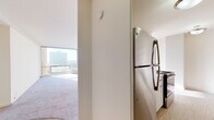 This well-appointed 2-bedroom, 1-bathroom residence spans a comfortable footprint across a single floor, offering a thoughtful layout designed for everyday living. The galley-style kitchen is efficiently organized with white cabinetry, granite-look countertops, a stainless steel refrigerator, an electric range, a dishwasher, and a single-basin sink — providing ample workspace and storage for home cooking. Wood-look flooring runs through the kitchen, adding warmth and easy maintenance underfoot. The living area is bathed in natural light through large floor-to-ceiling windows that frame expansive city and treetop views, creating a bright and airy atmosphere. The bedrooms feature plush carpeting and generous closet space, including a walk-in style closet with built-in wire shelving for organized storage. The full bathroom is finished with grey subway tile surrounding a soaking tub and shower combination, a white vanity with cabinet storage, a mirrored medicine cabinet, and warm-toned fixtures. Neutral wall tones and clean lines throughout the residence create a calm, cohesive aesthetic that is both functional and move-in ready.