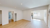 This single-floor unit showcases a clean, modern aesthetic defined by crisp white walls, light hardwood flooring, and recessed lighting throughout. The open living area is generously proportioned, with recessed ceiling lights casting an even glow across the space. A wall-mounted heater and a convenient closet are also found in this area.

The kitchen is thoughtfully designed with white shaker cabinets, black hardware, light stone countertops, a subway tile backsplash, and a full suite of stainless steel appliances including a gas range and refrigerator. A turquoise dishwasher adds a distinctive pop of color. Overhead flush-mount lighting completes the functional layout.

The bedrooms are bright and well-sized, each fitted with ceiling fans and windows that invite natural light and outdoor views. The primary bedroom features dual closets, providing ample storage. Additional rooms maintain the same minimal, airy character with light hardwood floors and white walls.

The bathroom is finished in a clean, contemporary style with white subway tile surrounding the tub and a sliding glass shower door. A white vanity with a stone countertop, mirror, and modern light fixture complete the space. A stacked washer and dryer unit is conveniently located within the bathroom, adding practical in-unit laundry access.
