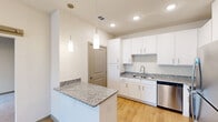 Located at 691 Union Chapel Rd in Cedar Creek, TX, this one-bedroom, one-bathroom unit offers a thoughtfully designed single-floor layout that makes smart use of every square foot. The kitchen serves as the centerpiece of the living space, showcasing crisp white shaker cabinetry that extends to the ceiling, speckled granite countertops, and a full suite of stainless steel appliances including a refrigerator, range, microwave, and dishwasher. A peninsula with a matching granite surface provides additional prep space and doubles as a casual dining area, while two pendant lights hang overhead to create a warm, focused ambiance. Light wood-style flooring flows throughout the main living areas, lending a clean and contemporary feel. The bedroom is accessed through a distinctive sliding barn door, adding a modern farmhouse touch to the interior. The carpeted bedroom offers a quiet, cozy retreat with ample wall space. A dedicated closet provides organizational convenience. The bathroom is finished with a full tub and shower combo, white tile surround, wood-style flooring, and an overhead cabinet for storage. Recessed lighting and neutral wall tones throughout the unit create a bright, cohesive atmosphere well-suited to comfortable everyday living.