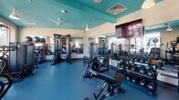 The Six Points Bloomfield Fitness Center is a thoughtfully designed, single-floor facility in Bloomfield, NJ, offering a comprehensive workout environment for residents and members. The space is immediately distinguished by its bold teal ceiling, which contrasts with cream-toned walls and a durable blue rubber flooring—creating a vibrant yet functional aesthetic throughout.

The fitness floor is organized to accommodate a wide range of training styles. A dedicated free weights area features a full rack of dumbbells alongside adjustable benches and a cable/functional trainer system, supported by floor-to-ceiling mirrors that enhance the sense of space. Ceiling fans and recessed lighting provide comfortable conditions during workouts.

The cardio zone is positioned near large windows that offer panoramic views of the surrounding Bloomfield streetscape, flooding the area with natural light. Equipment here includes treadmills, stair climbers, stationary bikes, and vertical climbers. A mounted flat-screen TV adds an entertainment option for users.

Additional amenities include a water fountain station, storage cubbies, and a wall-mounted TV in the strength training area. The overall ambiance is clean, energetic, and modern, combining practical fitness infrastructure with an inviting design that encourages an active lifestyle.