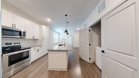 Located at 2908 Grand Cypress Dr in Lutz, FL, this well-appointed 1-bedroom, 1-bathroom unit offers a thoughtfully designed single-floor layout. The open-concept kitchen serves as the centerpiece of the living area, featuring a large central island with a built-in sink, sleek gray quartz countertops, crisp white cabinetry with matte black hardware, a geometric tile backsplash, and a full suite of stainless steel appliances including a range, over-the-range microwave, and refrigerator. Pendant lighting above the island adds a modern, polished touch. Wood-look plank flooring flows through the kitchen, living, and entry areas, lending warmth and visual continuity throughout the main living space. The bedroom is a comfortable retreat, finished with plush carpet, a ceiling fan, and a window with blinds that allows natural light to fill the room. A dedicated closet provides organized storage. The bathroom is cleanly finished with a tub-shower combination featuring full tile surround, wood-look flooring, white cabinetry, and gray countertops. In-unit laundry hookups are also present. The clean, neutral palette and modern finishes throughout create a bright, cohesive ambiance well-suited for contemporary living.