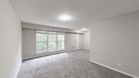 Located at 1301 Canal Dr in Chesapeake, VA, this single-floor, two-bedroom, one-bathroom home offers a practical and comfortable layout. The galley-style kitchen is a standout feature, equipped with slate-grey cabinetry, granite-look countertops, a double stainless steel sink, and white appliances including a range, microwave, and refrigerator. Warm wood-look flooring runs throughout the kitchen, adding a clean, modern contrast to the cabinetry. A hallway connects the main living areas and leads to the bedrooms and bathroom. The spacious primary bedroom offers generous square footage, soft carpeting, and ample natural light, while the second bedroom also features plush carpet and a window overlooking the greenery outside. Both rooms are finished with neutral, warm-toned walls and clean white trim, creating a calm and inviting atmosphere. The dedicated closet includes built-in shelving and hanging rods, providing well-organized storage. The bathroom is outfitted with a full tub-shower combo featuring classic white subway tile surround, a toilet, and a vanity mirror. Throughout the home, the consistent neutral palette and carpeted living spaces contribute to a cozy, move-in-ready feel.