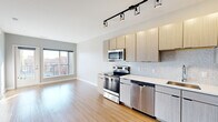 Located on South Grand Boulevard in the vibrant Tower Grove neighborhood of St. Louis, this contemporary single-floor unit offers a well-designed layout with modern finishes throughout. The kitchen serves as a standout feature, outfitted with light wood-grain flat-panel cabinetry extending to the ceiling, a white hexagon tile backsplash, sleek white countertops, and a full suite of stainless steel appliances including a refrigerator, range, microwave, and dishwasher. Track lighting overhead adds both function and a modern aesthetic touch. The open-concept layout connects the kitchen seamlessly to the living area, which is bathed in natural light from large windows and a glass door leading to a private balcony with views of the surrounding neighborhood. Light hardwood-style flooring runs throughout the main living spaces, lending warmth and continuity. The bedrooms feature plush carpeting, ceiling fans, and generous windows that frame views of the cityscape, filling each room with natural light. One bedroom includes a dedicated closet with built-in shelving. The bathroom is finished with clean white tile, a glass-enclosed shower, and warm wood-tone flooring, offering a crisp, modern feel. The neutral gray palette used throughout the unit creates a calm and cohesive atmosphere.