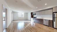 Located on Wilshire Boulevard in the heart of Los Angeles, this single-floor unit offers a well-designed, modern living space with a clean, contemporary aesthetic throughout. The open-concept layout seamlessly connects the living area to the kitchen, creating a bright and airy atmosphere enhanced by large windows dressed with vertical blinds that invite generous natural light across the gleaming hardwood-style flooring.

The kitchen is thoughtfully appointed with two-tone cabinetry — combining sleek gray upper cabinets with rich wood-grain lower cabinets — complemented by a crisp white countertop and a full suite of stainless steel appliances, including a refrigerator, electric range, microwave, and dishwasher. Recessed lighting overhead adds a polished finishing touch.

The living area is expansive and open, offering flexible space for various furniture arrangements, while the bedroom features plush carpeting and a sliding glass door that opens to a private balcony with glass railing panels, providing views of the surrounding urban environment.

The bathroom is finished with wood-look tile flooring, vertical tile surround in the tub/shower combination, and clean white fixtures, reflecting the same modern sensibility carried throughout the unit. Overall, the space delivers a bright, functional, and contemporary living environment in a prime Los Angeles location.