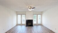 This 2-bedroom, 2-bathroom residence in Columbia, SC offers a well-planned single-floor layout with a thoughtful mix of updated finishes and comfortable living spaces. The open living room serves as the heart of the home, showcasing wood-style plank flooring, a black-surround fireplace as a central focal point, and a ceiling fan with light fixture overhead. Large windows flanking the fireplace flood the room with natural light and provide views of the surrounding greenery, with access to an outdoor balcony. A pass-through shelf connects the living area to the kitchen, which features gray cabinetry, white quartz-style countertops, a stainless steel sink, and a clean white subway tile backsplash with an open wood floating shelf — giving the space a modern, refreshed aesthetic. Both bathrooms are updated with gray vanities, quartz countertops, large mirrors, and tub-shower combinations with white tile surrounds and wood-style flooring. The two bedrooms are carpeted and filled with natural light from windows with blinds, offering a quiet and comfortable retreat. Additional storage is provided through two closets and a utility room, rounding out this efficiently designed and well-appointed home.
