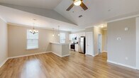 This single-story home in Biloxi, Mississippi offers a well-designed open-concept layout that seamlessly connects the living, dining, and kitchen areas. The living room is a standout space, featuring soaring vaulted ceilings, warm wood-look flooring, a sleek electric fireplace, and a ceiling fan that enhances both comfort and style. Natural light filters in through multiple windows, brightening the neutral-toned walls throughout.

The kitchen is thoughtfully appointed with crisp white shaker cabinetry, stainless steel appliances including a refrigerator, range, and over-the-range microwave, and a peninsula that provides additional prep and seating space. Pendant lighting and a chandelier add decorative touches to the open dining area nearby.

The bedrooms are carpeted for comfort, each equipped with ceiling fans and ample natural light from well-placed windows. Storage is addressed with walk-in closet space in at least one bedroom. The bathrooms are clean and functional, featuring tub-shower combos with tiled surrounds, white cabinetry, and light wood-look flooring. A stairwell with white railings and a bright window adds an architectural detail to the interior. The home's cohesive neutral palette and modern finishes create a clean, move-in-ready atmosphere throughout.