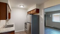 Located at 540 W Alexis Rd in Toledo, Ohio, this single-floor unit offers a practical and efficient layout across two bedrooms, one bathroom, a living room, and a kitchen. The living room features wood-look vinyl plank flooring, neutral gray walls, a large window with blinds that invites natural light, and a wall-mounted AC unit. A dark-paneled bifold closet door adds a contrasting design element. The kitchen is outfitted with rich, warm-toned cabinetry, stainless steel appliances including a refrigerator and range, a granite-look countertop, and wood-look flooring that flows seamlessly from the living area. Both bedrooms are finished with plush wall-to-wall carpeting, neutral paint tones, and windows with blinds that bring in outdoor views. Each bedroom features dark bifold closet doors for storage. Baseboard heating units are present throughout the bedrooms, ensuring year-round comfort. The bathroom is clean and functional, featuring wood-look tile flooring, a full tub-shower combination, a pedestal sink area, a dark-toned vanity, and a ventilation fan. Textured ceilings are consistent throughout the unit, contributing to its understated residential character.