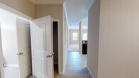 Located on Praxis Way in Cary, NC, this single-floor residence offers a thoughtfully designed layout that balances comfort and functionality. The kitchen is a standout feature, showcasing rich dark-stained wood cabinetry, dark countertops, and black appliances including a range, built-in microwave, and refrigerator, all set atop clean tile flooring. A hallway connects the main living areas, finished with tile underfoot and crown molding overhead, lending a polished, cohesive aesthetic throughout. Decorative columns provide an elegant transition between spaces.

The living area is generously sized, carpeted for warmth and comfort, and fitted with a ceiling fan and crown molding. Large windows and a glass-paned door flood the room with natural light while providing direct outdoor access. The bedroom continues the neutral, calming palette with soft carpet, crown molding, and ample wall space. A walk-in closet with built-in shelving offers practical storage. The bathroom includes a tiled tub-shower combination with built-in shelving, tile flooring, and clean, functional finishes throughout. Overall, the space presents a clean, move-in-ready environment with consistent design details across every room.