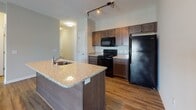 Located at 24015 Crab Apple Ct in Georgetown, Delaware, this single-floor residence offers a well-designed open-concept layout with contemporary finishes throughout. The kitchen serves as a central hub of the home, showcasing rich dark-stained cabinetry, granite countertops, a center island with a built-in sink, and a full suite of black appliances including a range, over-the-range microwave, and refrigerator. Durable hardwood-style flooring extends through the kitchen and into the open living area, which is illuminated by track lighting overhead and filled with natural light from large sliding glass doors that lead to the outdoors. The spacious living area provides a bright and airy atmosphere ideal for both relaxing and entertaining. Two generously sized bedrooms feature plush carpet flooring and ample natural light from large windows with outdoor views. The home includes two bathrooms — one with a walk-in shower and the other with a shower-tub combination — both finished with dark vanity cabinetry, white countertops, and modern chrome light fixtures. The neutral color palette and clean architectural lines throughout lend the space a cohesive, move-in ready aesthetic.