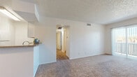 This 2-bedroom, 2-bathroom unit is thoughtfully laid out across a single floor, making efficient use of its space. The living room serves as the heart of the home, featuring plush carpeting, a tiled fireplace with a classic mantle, and a large sliding glass door dressed with vertical blinds that invites natural light and provides an outdoor view. Adjacent to the living area, the kitchen is equipped with white cabinetry, a granite-style countertop, white appliances including a range and refrigerator, and a peninsula that opens toward the living space — ideal for casual dining or entertaining. The textured ceilings are consistent throughout. A hallway connects the remaining rooms, including two carpeted bedrooms, each featuring ceiling fans and ample natural light from windows with blinds. The primary bedroom includes access to a dedicated walk-in closet outfitted with built-in shelving and hanging rods on multiple walls, offering generous storage. Both bathrooms feature stone-tone countertops, white cabinetry, large mirrors, and tile flooring. The overall aesthetic is clean, neutral, and move-in ready, with a consistent color palette of whites and warm beiges throughout.