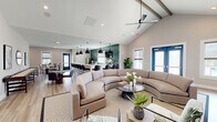 Located at 609 Grove Circle in Milton, Delaware, this single-floor space offers an expansive, open-concept layout combining a living room and kitchen into one cohesive, well-appointed area. The architectural centerpiece is the dramatic vaulted ceiling, which rises to a striking peak and is fitted with a skylight that floods the interior with natural light. Wide-plank light hardwood flooring runs throughout, lending warmth and continuity to the space.

The living area is generously proportioned, anchored by a curved sectional sofa, a built-in media center with natural wood cabinetry, and a shiplap-framed fireplace that adds a coastal-contemporary character. Bold blue double doors open outward to an outdoor area, flanked by windows with woven roman shades that frame outdoor views. A ceiling fan with exposed beam detailing completes the airy feel.

The kitchen is defined by an eye-catching emerald green hexagonal tile backsplash that extends to the ceiling, contrasting beautifully with white quartz countertops and light wood cabinetry. A large island with leather bar seating and black pendant lighting serves as a social hub. Stainless steel appliances, ample counter space, and a secondary seating and dining area make this kitchen as functional as it is visually striking. A quieter sitting area with French doors rounds out the layout.