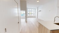 Located at 1 Lyon Pl, Unit 1H in White Plains, NY, this thoughtfully designed residence offers a clean, modern aesthetic across a single floor with four distinct spaces. The open-concept living and kitchen area is anchored by a sleek island with light wood cabinetry and a white quartz countertop, complemented by stainless steel appliances including a refrigerator, range, and microwave. A glass tile backsplash and ample upper and lower cabinetry complete the well-appointed kitchen. Light hardwood flooring flows throughout, enhancing the bright, airy ambiance. Large floor-to-ceiling windows in the living and bedroom areas flood the space with natural light and provide open views of the surrounding streetscape. The rooms are finished with crisp white walls and feature wall-mounted split HVAC units for year-round climate control. The bathroom stands out with dramatic full-height marble-style tile surrounding the soaking tub and shower, paired with a modern wood-framed vanity, mirrored medicine cabinet, and clean white fixtures. The overall design emphasizes minimalism and functionality, creating a cohesive, contemporary living environment in the heart of White Plains.